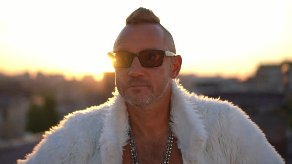 Thoughtful Adult Man in White Fur Coat and Sunglasses Standing in Sunshine Outdoors Looking Away