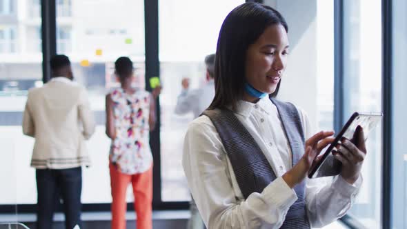 Portrait of asian woman with face mask around her neck using digital tablet at modern office