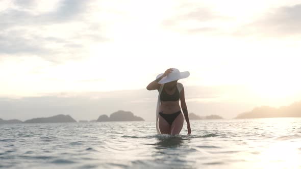 Woman In Bikini Walking In Sea As Sun Sets