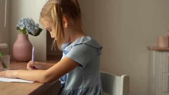 Side View of Focused Creative Girl Child Drawing with Pen Making Picture Sitting at Table in Light