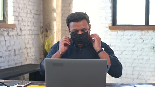 Indian Man Puts on Protective Facial Mask Sitting on the Workplace in the Office