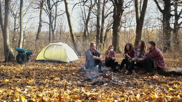 Tourists having hot drinks by fire in autumn forest