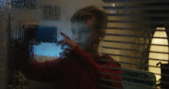 Boy Filming Storm Through Window