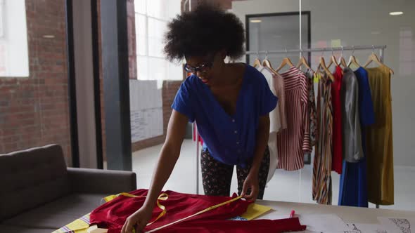 African american female fashion designer taking measurements of clothing with a tape measure