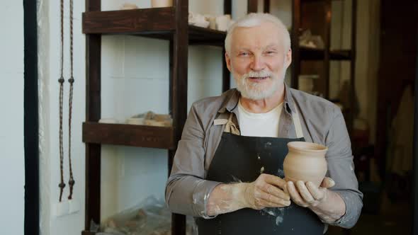 Portrait of Senior Potter in Apron Standing in Workshop Holding Pot Smiling