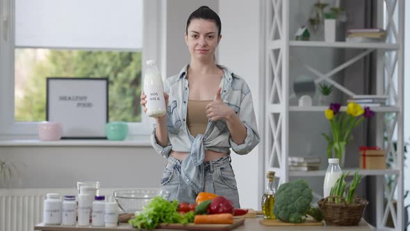 Confident Millennial Woman Showing Soy Milk Gesturing Thumb Up Smiling Looking at Camera