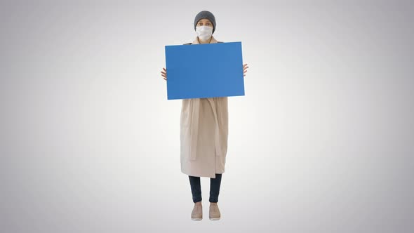 Woman in Outdoor Clothes and in Medical Mask Holding Blank Board on Gradient Background