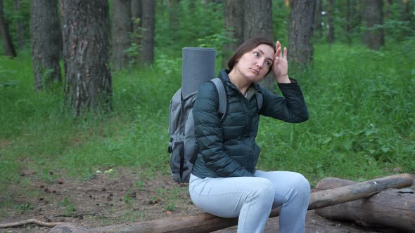 Young Woman in Hiking Clothes and with a Backpack Sits Tired in the Forest