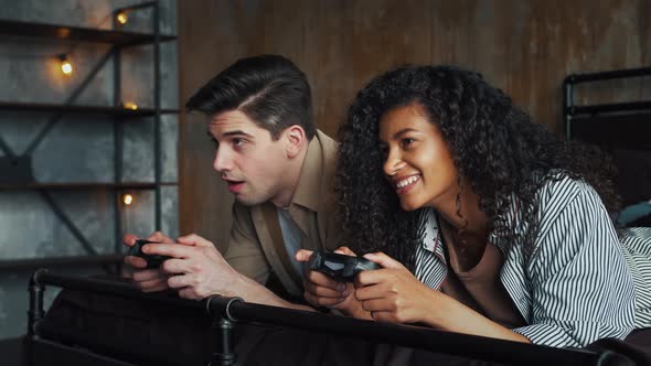 Excited Couple in Casual Clothes are Laughing Holding Wireless Gamepads and Playing Video Game on