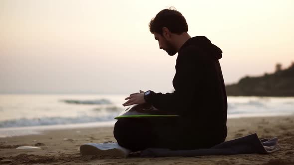 The Man Playing Hang Sitting on the Beach in Front the Sea Alone