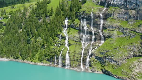 Cinematic aerial of multiple waterfalls streaming from mountain into blue lake