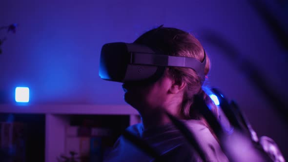 A girl wearing VR glasses stands in a dark room. Hands is making various gestures