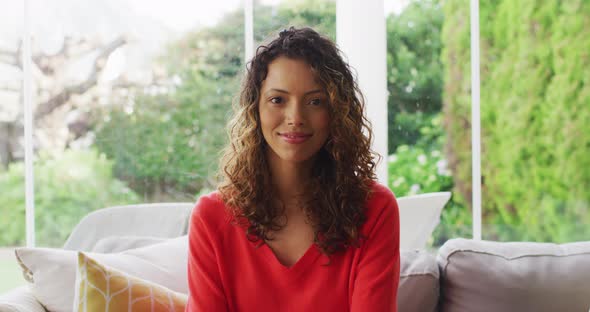 Portrait of biracial woman sitting on sofa, looking at camera and smiling