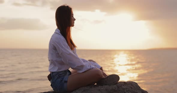 Young Woman Looks at the Sea Sunset Sitting on a Hill