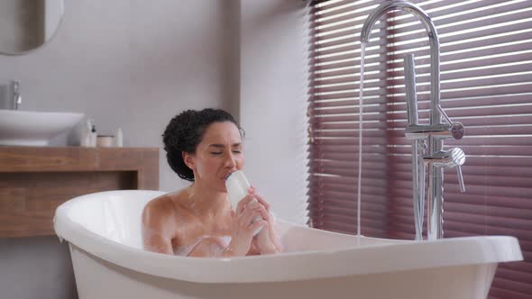 Funny Young Woman Sits in Foamy Bath Sings Using Shampoo Bottle As Microphone Enjoying Energetic