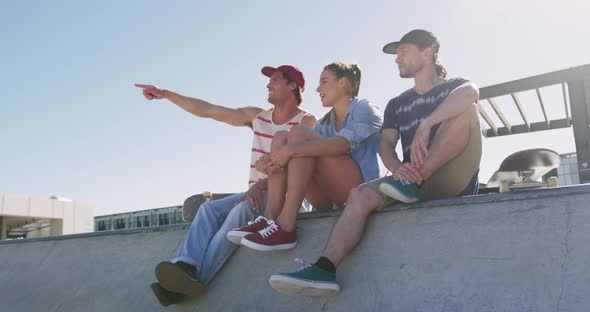 Caucasian woman and two male friends sitting talking and pointing something in distance on sunny day
