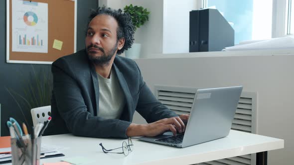 Pensive Middle Eastern Man Working with Laptop and Thinking Sitting at Desk in Office