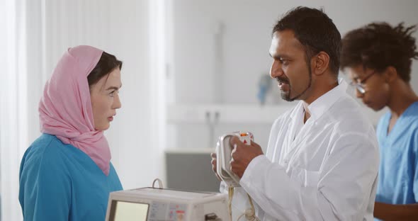 Side View of Indian Doctor Showing Young Muslim Nurse How to Use Defibrillator