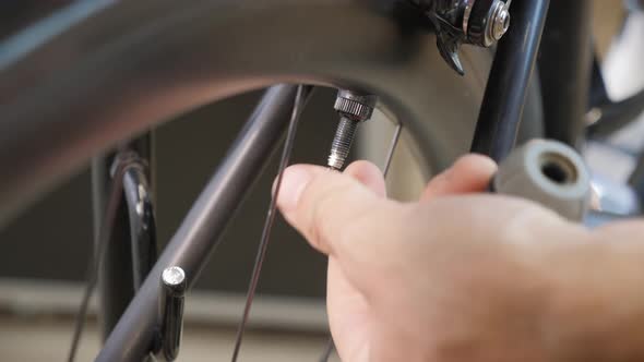 Male bicycle technician screwing cap from bike tire after pumping air into tire using bike pump. 