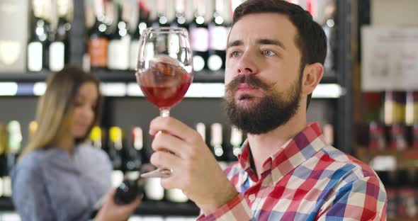 Close-up of Focused Caucasian Man Smelling Red Wine in Glass and Shaking Wineglass. Confident