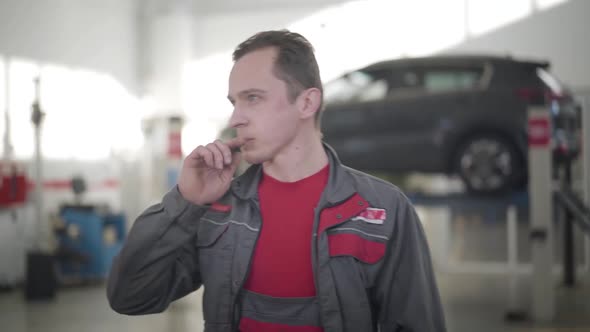 Young Male Auto Mechanic Looking Around in Repair Shop and Thinking. Portrait of Caucasian