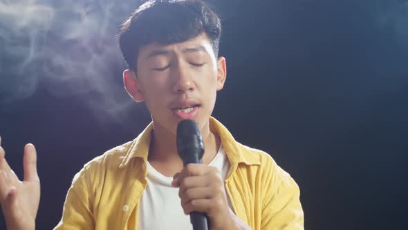 Close Up Of Young Asian Boy Holding A Microphone And Singing On The White Smoke Black Background