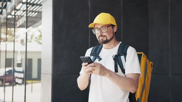 Happy Delivery Man Writes Text Messages on His Smartphone