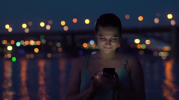 Girl Uses a Smartphone While Walking on a Night Beach