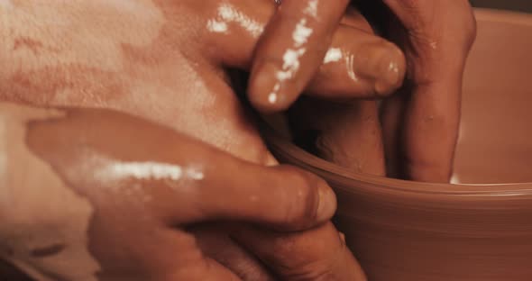 Hands of Couple Form a Pot of Clay on a Potter's Wheel. A Female Hand Helps a Man's Hands Shape a