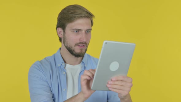 Young Man Reacting to Loss on Tablet on Yellow Background