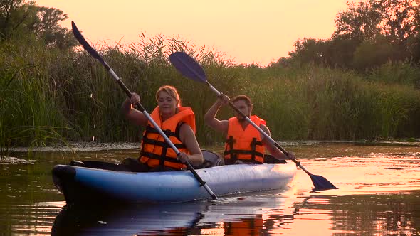 Two People in Rowing Oars Sitting in a Kayak on the Lake in the Sunset. Slow Motion