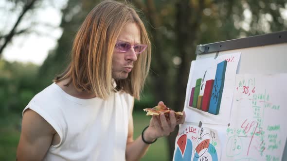 Focused Male Young Startuper Eating Pizza Writing on Whiteboard Outdoors in Summer Spring Park