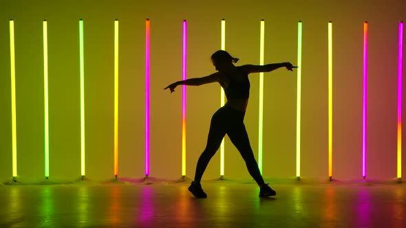 Young Woman Dancing in a Studio Illuminated By Multicolored Neon Tubes