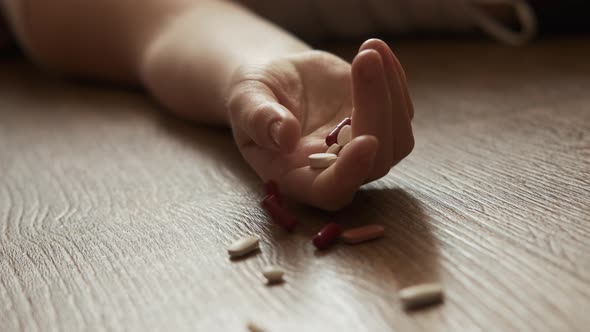 Woman Lying Unconscious on the Floor with Capsules in Her Hand