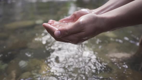 The hand grabbing the water from the stream. Slow motion.