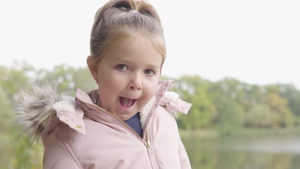 Cute Little Caucasian Girl Blows Kisses to the Camera in a Park  Closeup  a Lake in the Background