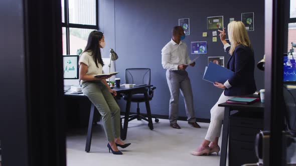 Diverse business people wearing face masks standing and talking in office