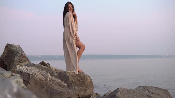 Sexy Girl Model Stands on Stones Against the Sea in a Long Dress