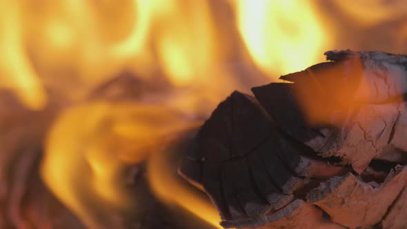 Close up of brightly burning wooden logs with yellow hot flames of fire at night.