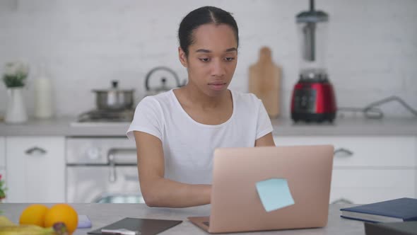 Young Woman Closing Laptop Taking Smartphone and Walking Away From Kitchen Table