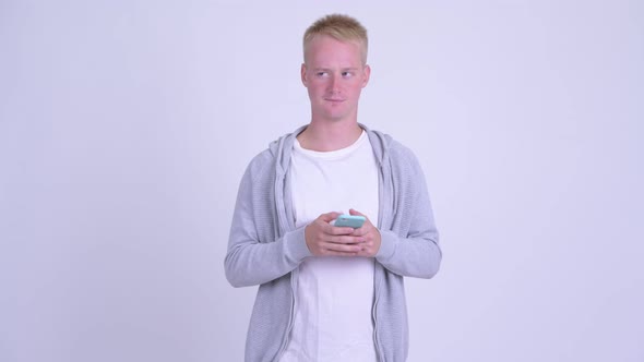 Happy Young Blonde Handsome Man Thinking While Using Phone