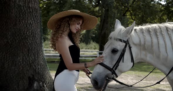 Beautiful Girl In A Hat Stroking A White Horse