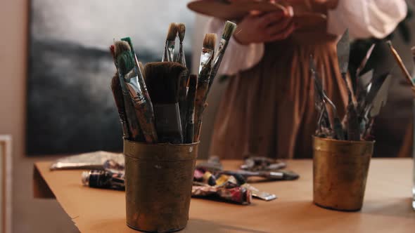 Art Studio  Young Woman Artist Changing Brushes From the Jar on the Table