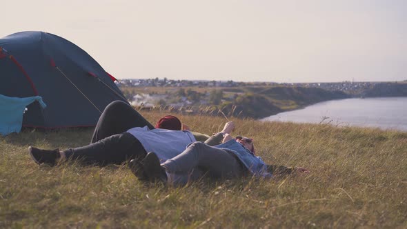 Woman Friends Rest Lying on Dry Grass By Tent on River Bank