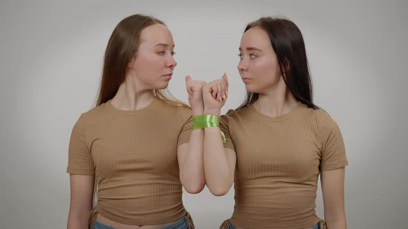 Twins with Serious Facial Expression Posing at Grey Background with Tied Hands