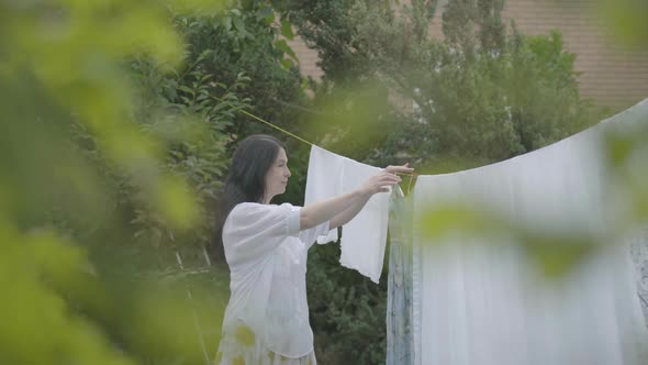 Back View of Attractive Woman with Long Hair Hanging White Clothes on a Clothesline Outdoors