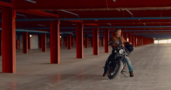 Biker Puts a Helmet on His Head Sits on a Motorcycle in a Large Garage