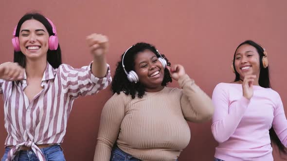 Happy young women having fun dancing and listening music with wireless headphones