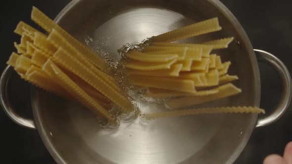 Man's Hands Putting Mafaldine Spaghetti Into a Steel Pan With Boiling Water