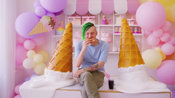 Young Man with Dreadlocks Eating Cake Sitting on Table in Confectionery